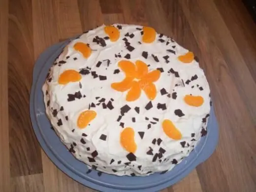 Eine dekorierte Zitronen-Mandarinen Torte liegt auf einem blauen Teller, umgeben von einem Holztisch. Schokoladenstückchen und Mandarinen zieren die Sahne.