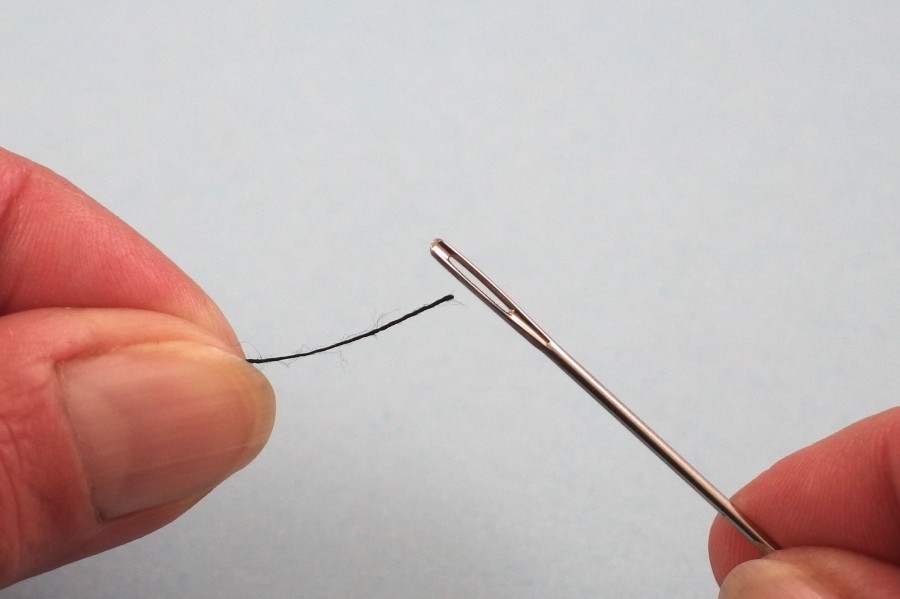 Faden über über einem kontrastierenden Blatt Papier durchs Nadelöhr leichter einfädeln.