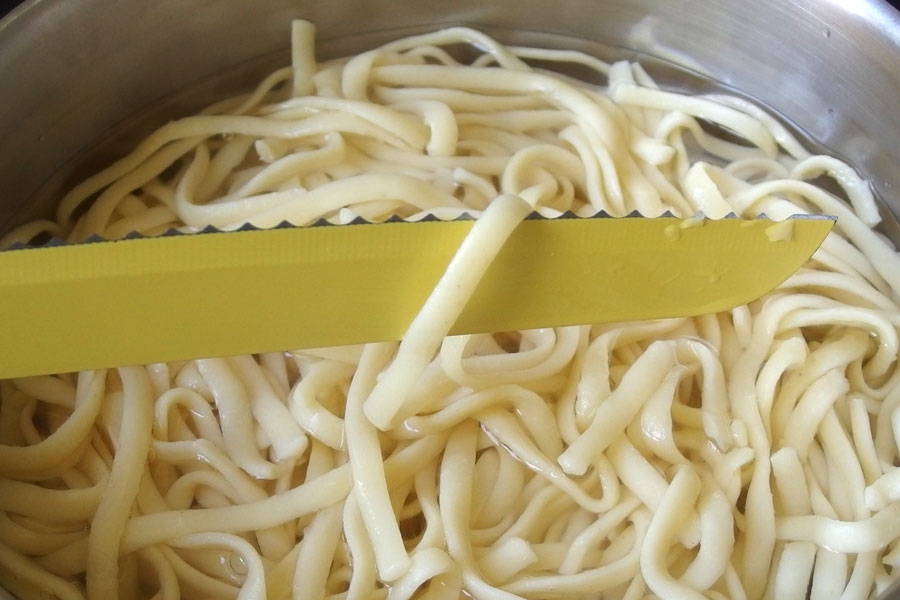 Mit einem gezackten Messer einzelne Spaghetti zur Garprobe aus dem Wasser heben.