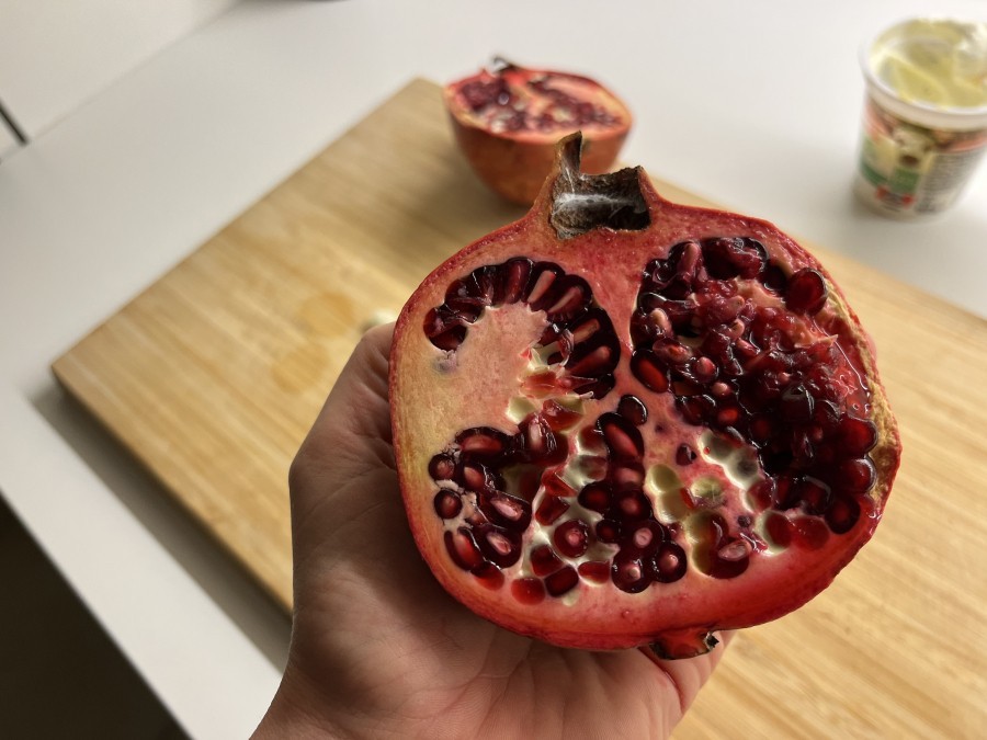 Man schneidet den Granatapfel durch und hält eine Hälfte mit dem Fruchtfleisch nach unten über eine Schüssel.