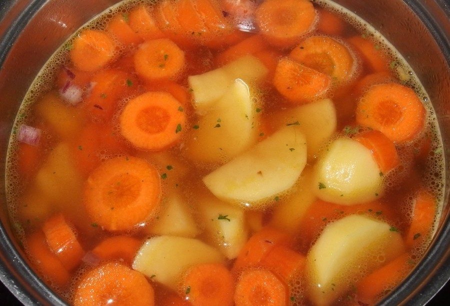 Kartoffeln und Karotten zu den Zwiebeln dazugeben, mit Gemüsebrühe aufgießen und 20 Minuten köcheln lassen.