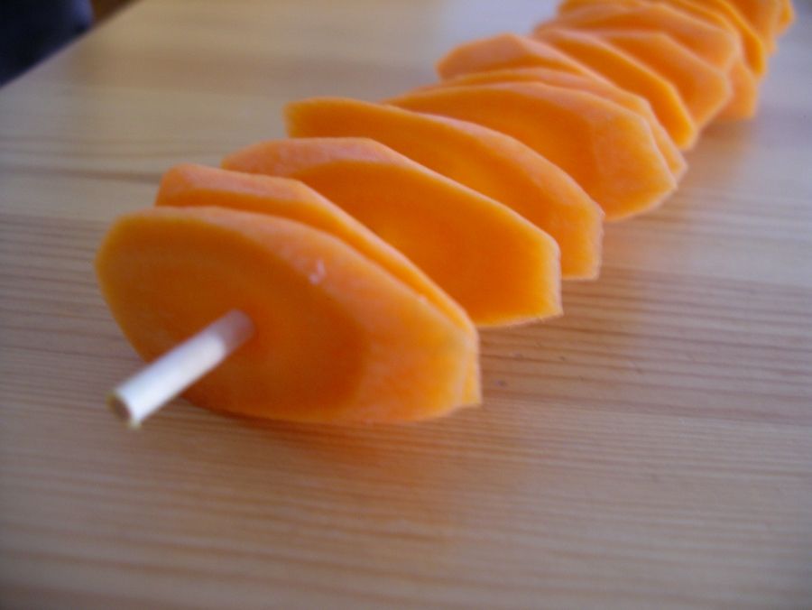 Sliced carrots are neatly arranged on a skewer, ready to be transformed into knusprige Möhrenchips im Backofen.