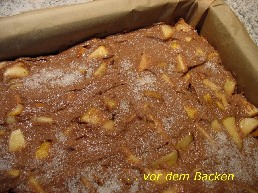 Ein Apfel-Kakao-Kuchen im Blech wartet vor dem Backen mit einer Zuckerschicht und zarten Apfelstückchen auf den Ofen.