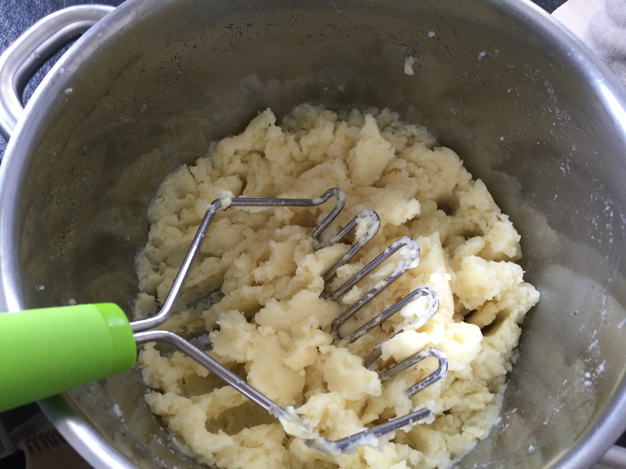 Kartoffeln werden mit einem Kartoffelstampfer zerdrückt