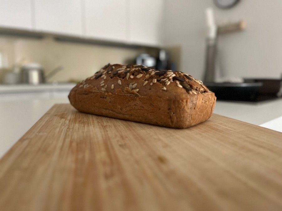 Ein frisch gebackenes Brot liegt auf einem Holzbrett in einer modernen Küche, umgeben von Küchengeräten.