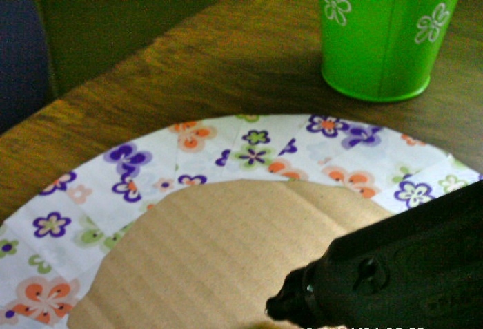 Das Blumentöpfchen auf der Unterseite der beklebten Pappplatte mit der Heißklebepistole oder dem Klebstoff fixieren.