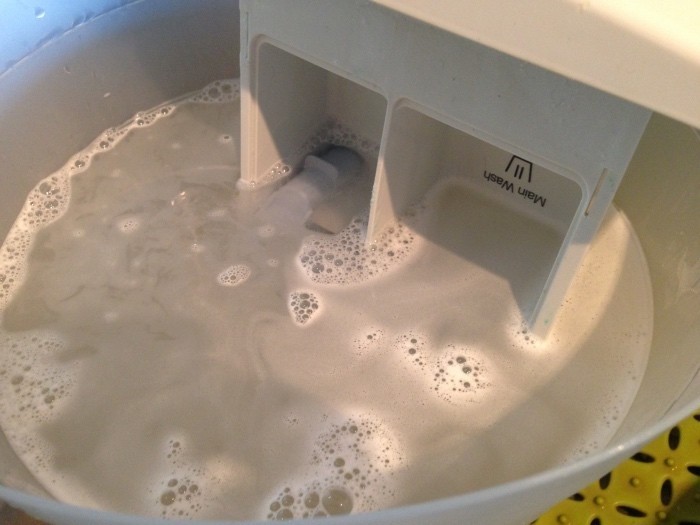 Einen Spültab löst man mit einem Schuss Essigessenz im heißen Wasser im Eimer auf und legt dann das Waschmittelfach hinein und lässt es einwirken.