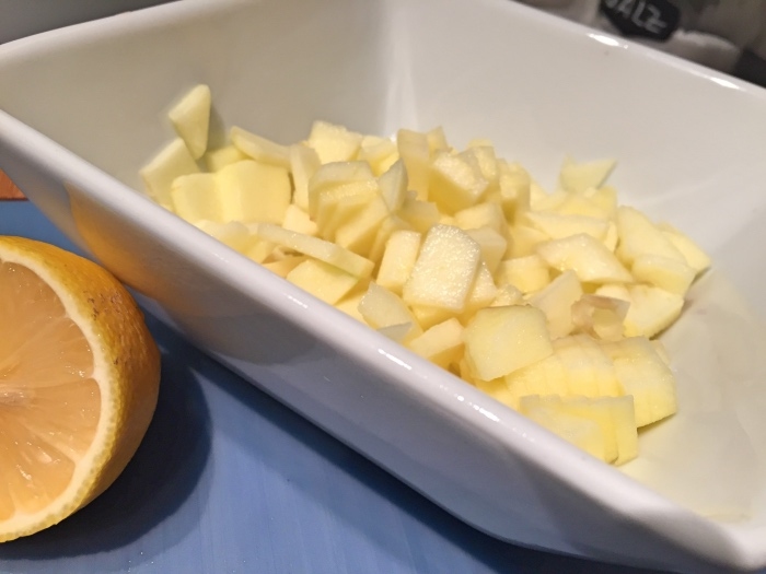 Der geschälte Apfel wird in Würfel geschnitten und in einer Schüssel sofort mit dem Zitronensaft verrührt.