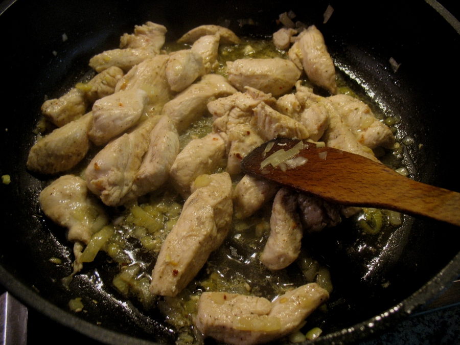 Hähnchenbrustfilet-Streifen mit Salz und Pfeffer gewürzt mit Zwiebelwürfeln und geriebenem Ingwer werden mit Olivenöl in der Pfanne angebraten.
