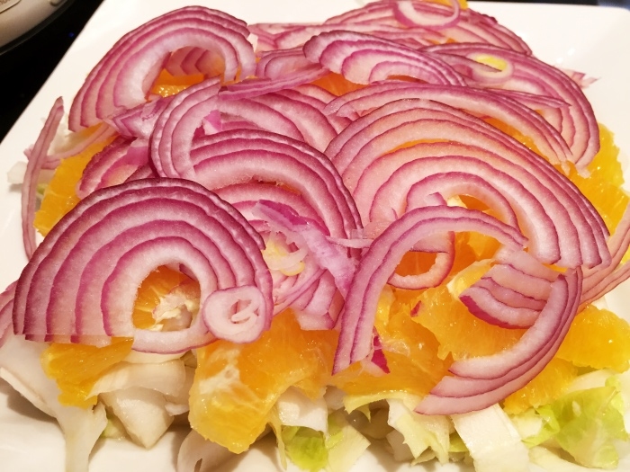 Salat auf einem Teller/Platte anrichten. Die Orangenscheiben und dann die Zwiebelscheiben darüberschichten.