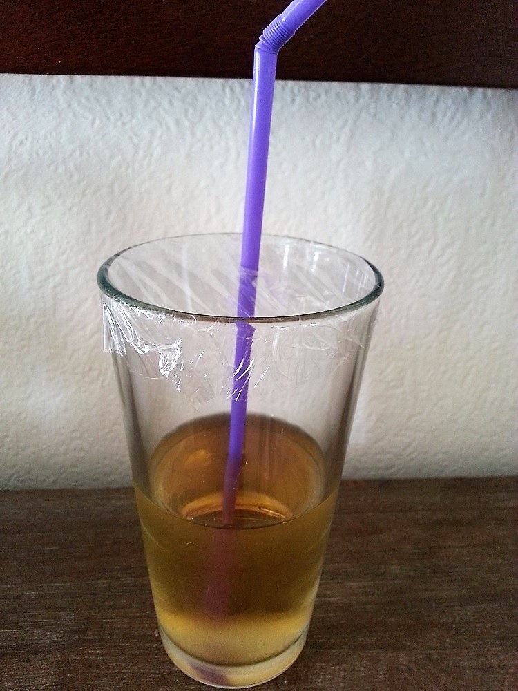 Ein Glas mit einem Getränk kann man ganz einfach mithilfe einer Frischhaltefolie vor Insekten und Schmutz schützen.
