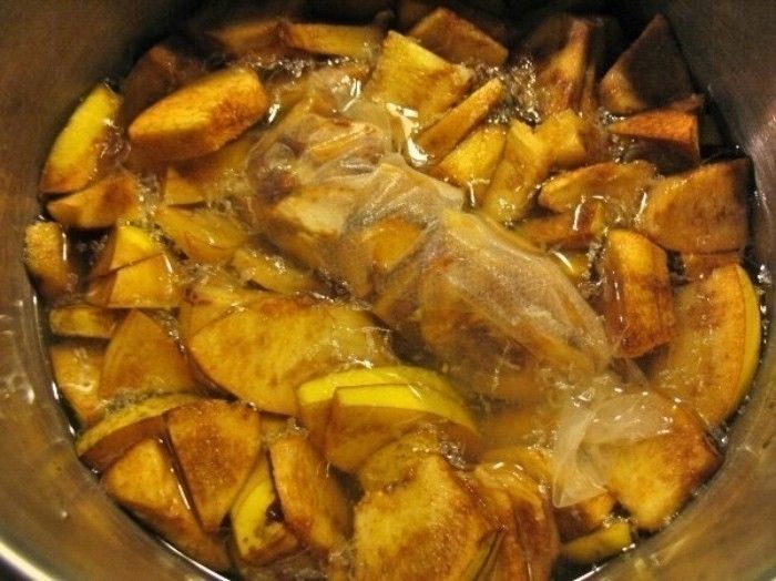 Quittenstücke kochen in einem Topf mit Wasser, während ein Stück Quittenbrot im Mittelgrund sichtbar ist.