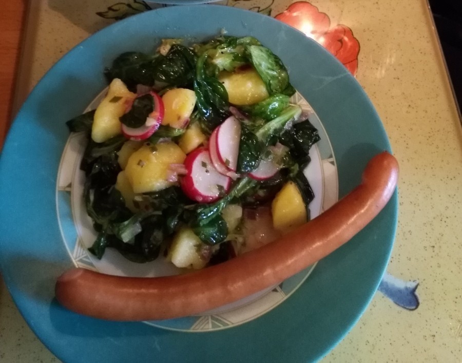 Der fertig zubereitete Kartoffelsalat "Radieselpunzel", auf einem Teller schön angerichtet, mit einem Wiener Würstchen.