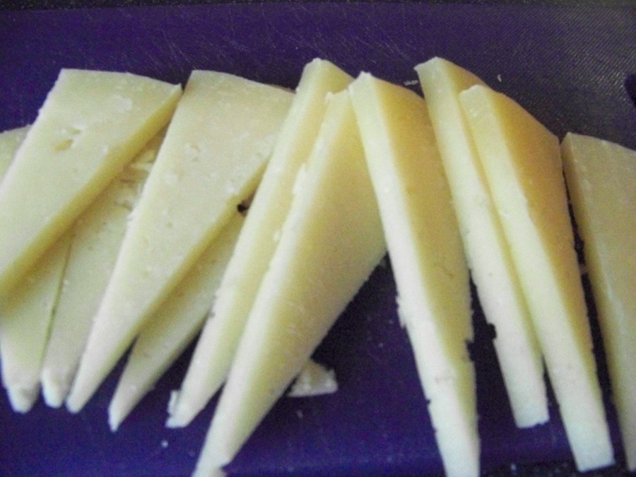 Den Manchego Käse entrinden und in ca. 5 mm Scheiben schneiden. Die Scheiben mit dem Fruchtgemisch bestreichen und mit Mandelsplitter bestreuen.