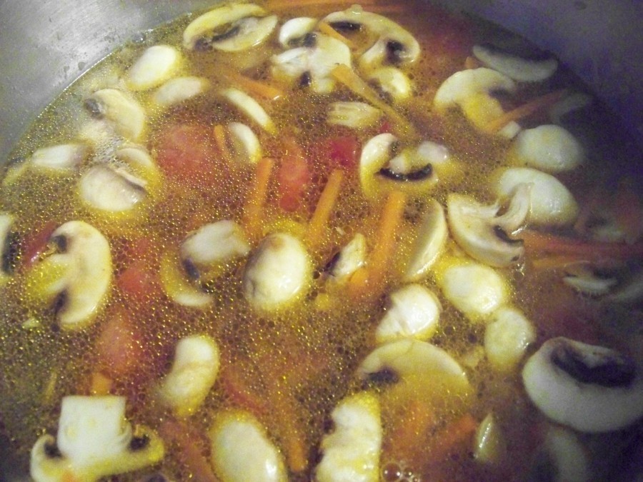 Die Champignons und die Tomaten hinzufügen, durchrühren und den Fond angießen, alles aufkochen lassen und ca. 3 Minuten kochen lassen.