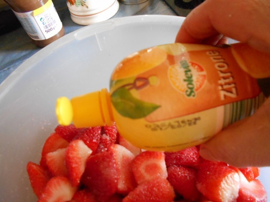 Die Erdbeeren putze und wasche sie. Ich viertele sie und gebe Zucker drauf und spritze Zitronensaft, etwa zwei bis drei Spritzer darüber.