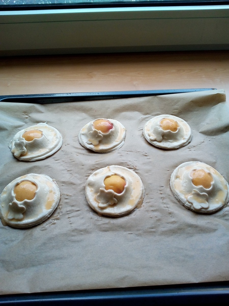 Jetzt wird der Rand der Teigplättchen mit Ei eingestrichen und weitere runde Teigteile ausgestochen. Diese werden dann in der Mitte nochmals mit einem kleinen Loch versehen und auf die Aprikosen aufgelegt. 