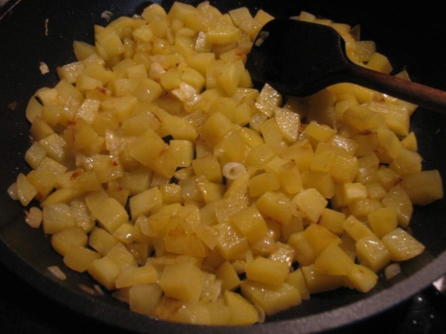 In einer großen Pfanne erhitzt man etwas Butterschmalz oder Öl, darin werden die Zwiebelwürfel glasig angedünstet. Dann gibt man die gewürfelten Kartoffeln dazu und unter ständigem Wenden werden sie goldbraun angebraten.