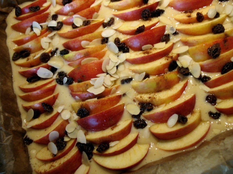 Der Teig wird mit den in schmale Spalten geschnittenen Äpfeln dicht belegt, mit Zimtzucker, Rosinen und Mandelblättchen bestreut.