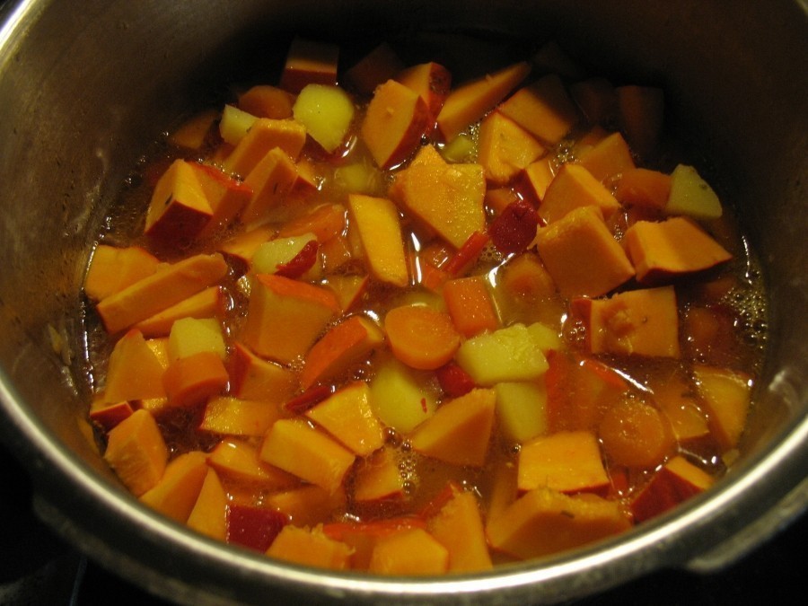 Karotten-, Kartoffel-, Paprikastücke und Kürbiswürfel werden in einem großen Topf gekocht.  