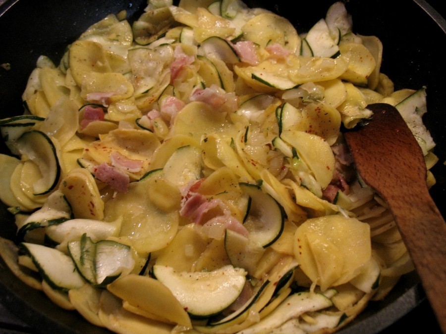 Zucchini- und Kartoffelwürfel werden mit den Paprikastückchen auf der heißen Pfanne mit Bacon und Zwiebelwürfeln goldbraun gebraten.