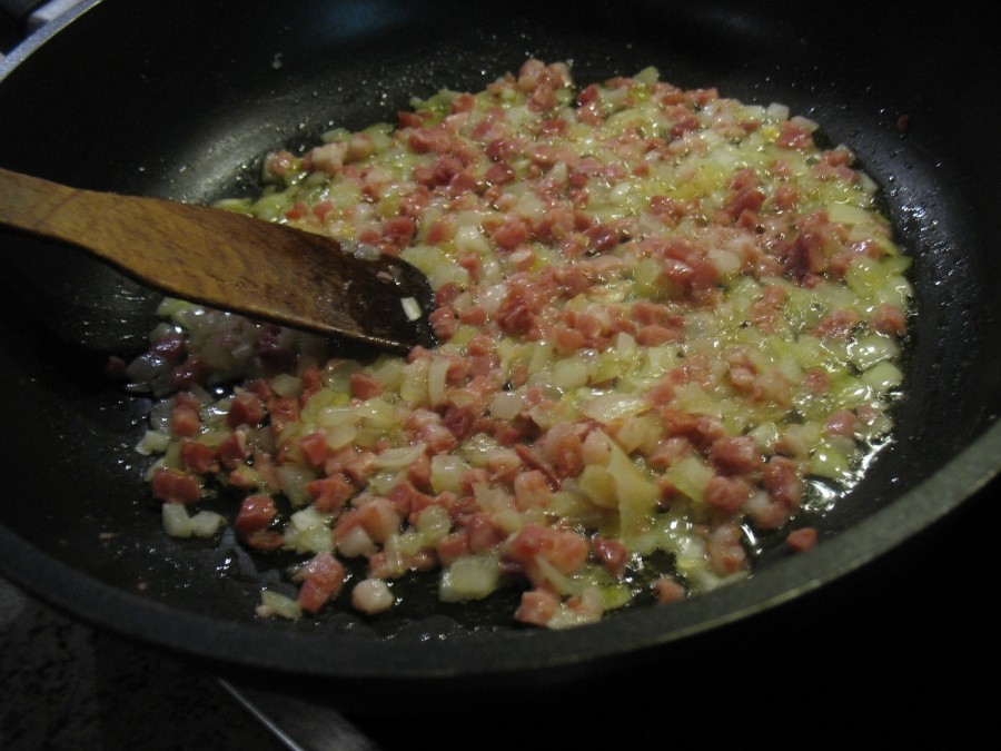 Zwiebelwürfel und Bacon (oder Schinkenwürfel) werden auf einer beschichteten Pfanne in dem heißen Öl glasig angedünstet.