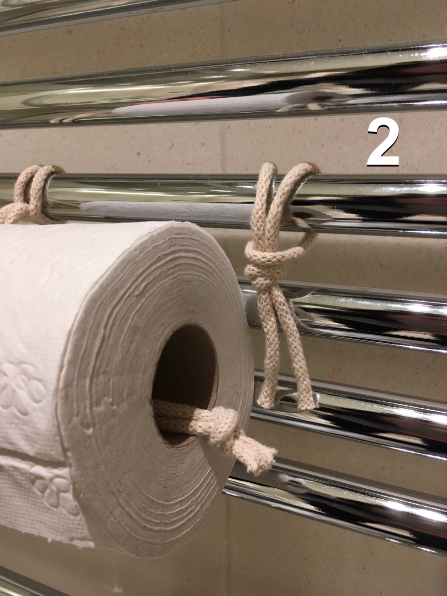 Sobald der Knoten der längeren Schlaufe durch die Toilettenpapierrolle geführt wurde und in das obere Stück der kurzen Schlaufe gesteckt wurde (Foto 3), wird das lange Ende fest nach unten gezogen (Foto 4), sodass die Schlaufe gut fixiert ist.