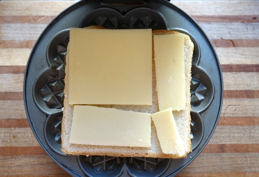 Das Waffeleisen öffnen und den Toast mit der gebutterten Seite auf das Waffeleisen legen. Den Käse drauflegen und den zweiten Toast mit der Butterseite nach oben auf den Käse legen.