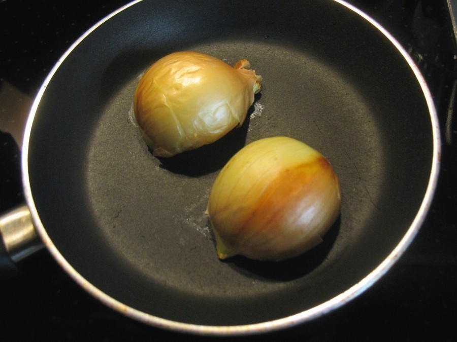 Eine Zwiebel wird mit der Schale halbiert und in einer Pfanne ohne Fett auf den Schnittstellen kräftig angeröstet.