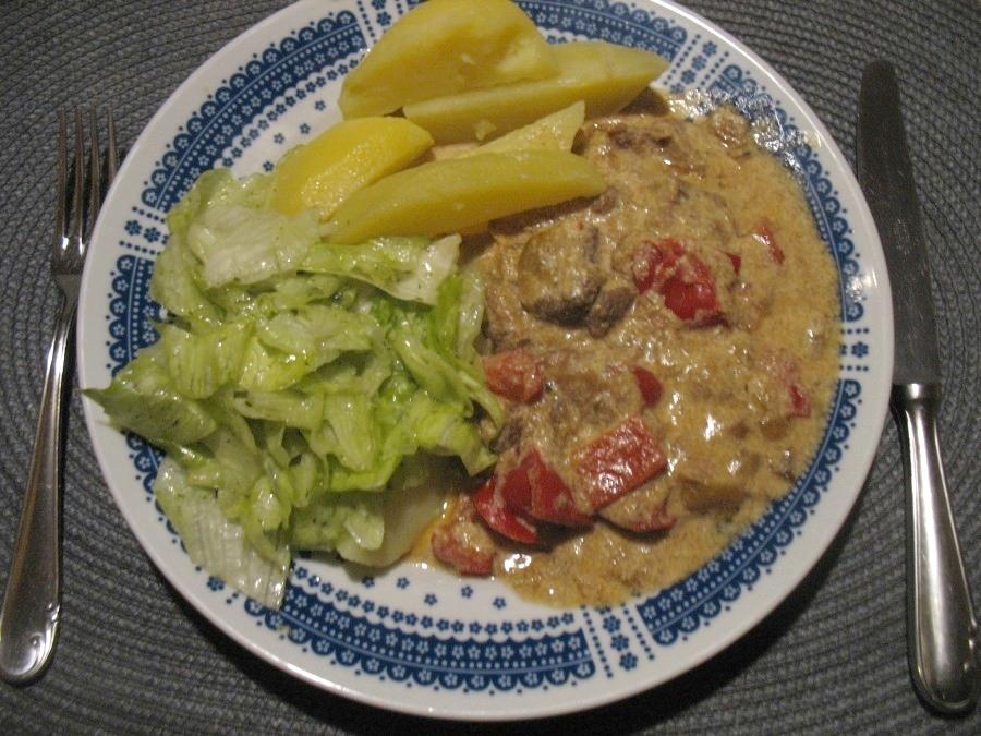 Hier das Paprika-Sahne-Gulasch mit Salzkartoffeln und frischem Salat auf einem Teller angerichtet.