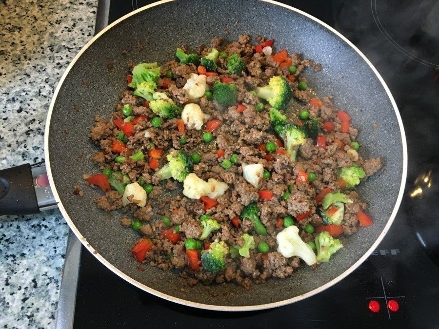 In einer Pfanne brät Hackfleisch mit TK-Gemüse, darunter Brokkoli und Blumenkohl, auf einem Herd.