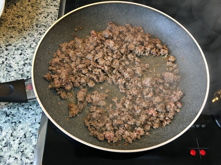 In einer Pfanne brät hackfleisch in eigenem Saft, umgeben von dunstiger Küchenatmosphäre. Ideal für Kartoffelkuchen.