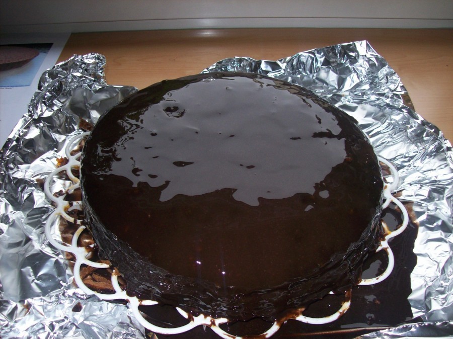 Die Glasur wird nun von der Mitte aus über den Kuchen gegossen und soll rundum über den Rand hinauslaufen, so dass die Torte insgesamt von der Schoko-Glasur umhüllt ist.