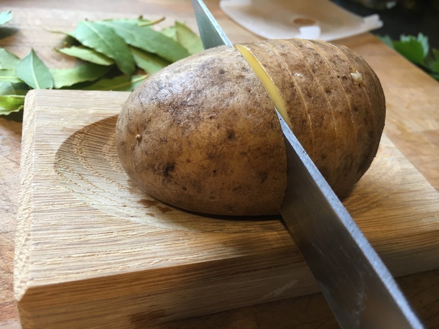 Jede Kartoffel mehrmals mit einem scharfen Messer so einritzen, dass sie unten noch zusammenhält. Am besten geht das, wenn man die Kartoffel in ein Holzbrettchen mit Mulde legt.
