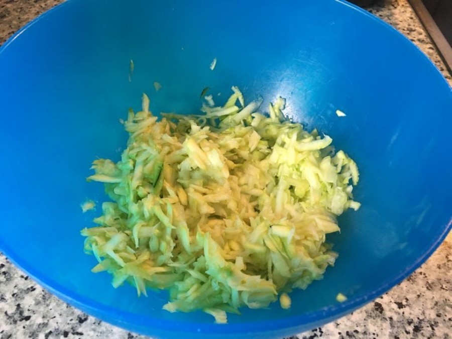 Zuerst die Zucchini waschen, schälen, grob raspeln und auf einem Küchenpapier verteilen. Die überschüssige Flüssigkeit mit den Händen und Küchenpapier von den Zucchini gut auspressen.