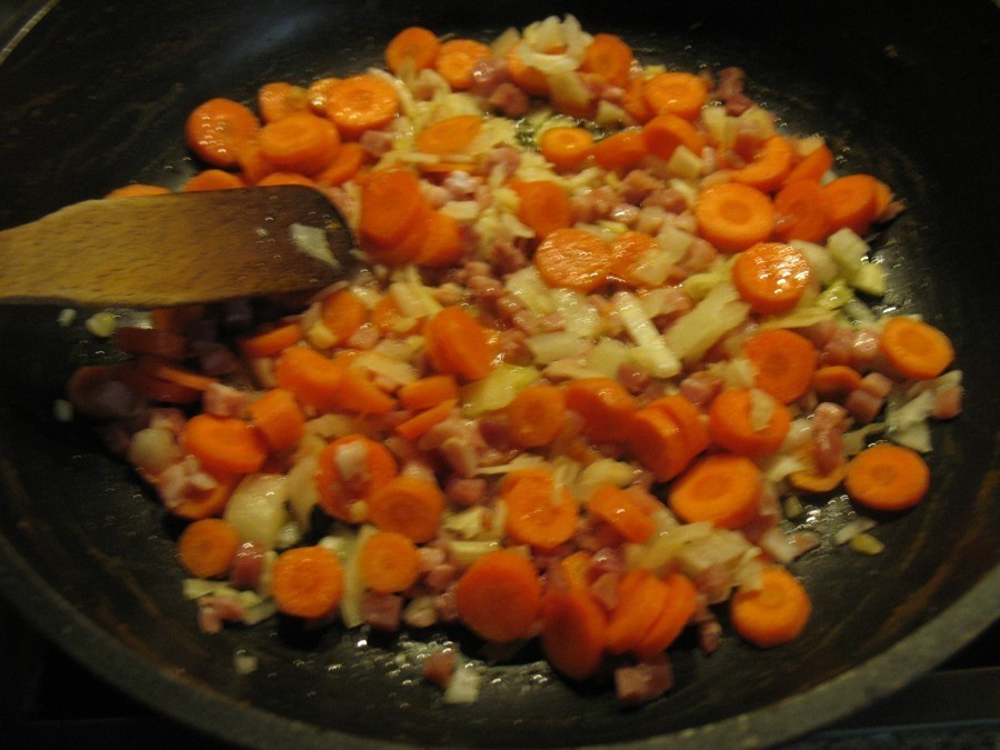 Zwiebel- und Knoblauchwürfel, Karottenscheiben und Schinkenwürfel werden in der Pfanne im heißen Öl bei mittlerer Hitze ca. zehn Minuten angebraten. 