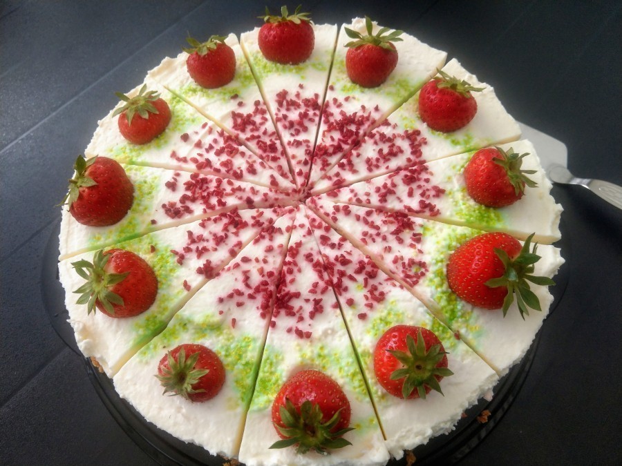 Torte verzieren: 12 ganze Erdbeeren mit grün in die Torte drücken. Ringsherum grünen Zucker verteilen und in die Mitte getrocknete Erdbeerkrümel streuen.