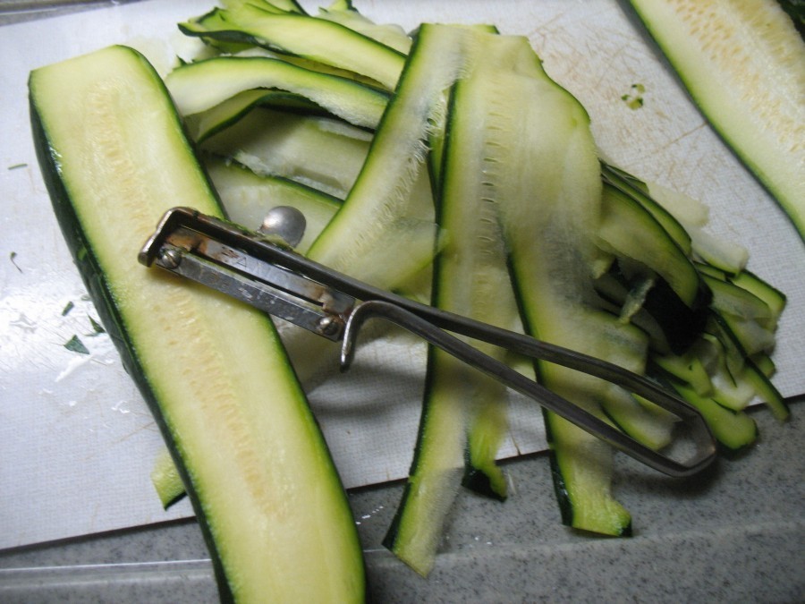 Die gewaschenen, geputzten Zucchini werden mit einem Sparschäler längs in dünne Streifen geschnitten. Die Reste sowie der Knoblauch werden gewürfelt.
