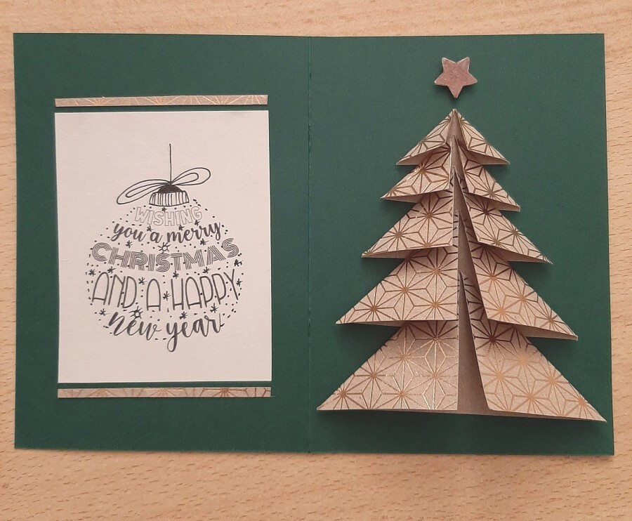 Die linke Hälfte einer Klappkarte sollte ein weihnachtlicher Gruß zieren, auf der rechten Hälfte ein aus Papier oder Karton gefalteter Tannenbaum den Blick auf sich ziehen. 