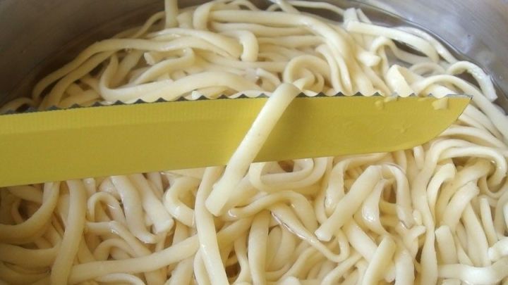 Mit einem gezackten Messer einzelne Spaghetti zur Garprobe aus dem Wasser heben.