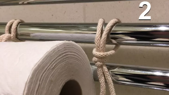 Sobald der Knoten der längeren Schlaufe durch die Toilettenpapierrolle geführt wurde und in das obere Stück der kurzen Schlaufe gesteckt wurde (Foto 3), wird das lange Ende fest nach unten gezogen (Foto 4), sodass die Schlaufe gut fixiert ist.