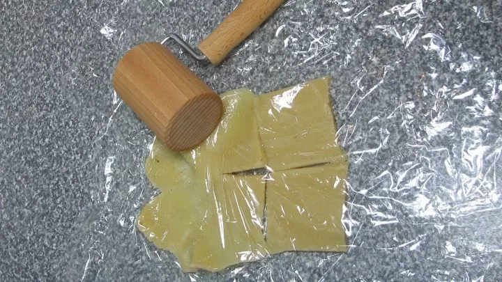 Die Marzipanrohmasse in dünne Scheiben schneiden und nebeneinander auf Frischhaltefolie legen. Eine zweite Lage Folie darüber ausbreiten und das Marzipan dünn ausrollen.