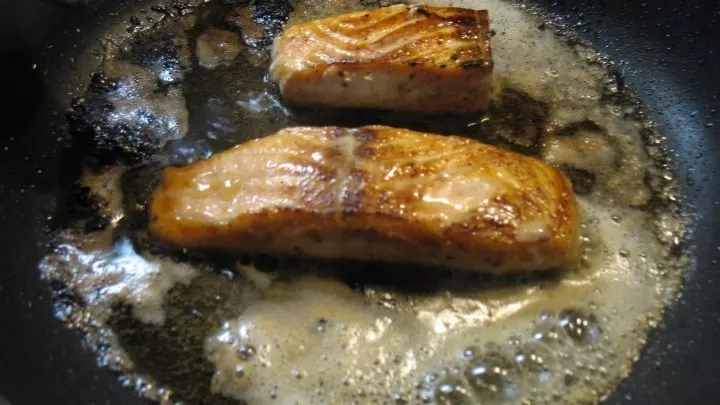 Nachdem der Lachs gewendet wurde und an den Seiten gar aussieht, wird er ab und zu mit heißer Butter übergossen und fertig gebraten.