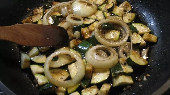 Die Zucchini wird gewaschen, geputzt und in kleine Stücke geschnitten. In der Pfanne werden die Zucchinistücke im erhitzten Olivenöl kurz angebraten und dann mit Zwiebelringen und Knoblauch unter Wenden bei mittlerer Hitze angedünstet.