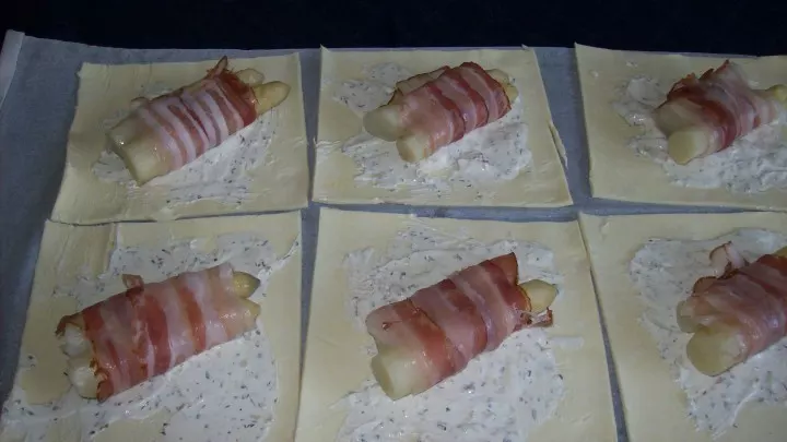 Die gleichgroß geschnittenen Spargelstangen werden nun, jeweils zwei Stücke, mit einer Scheibe Bacon umwickelt und auf die mit dem Frischkäse bestrichenen Teigplatten gelegt. 