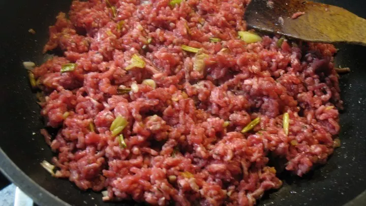In der Pfanne werden im heißen Öl Zwiebel und Knoblauch angedünstet, dann wird das gewürzte Hackfleisch krümelig angebraten. 