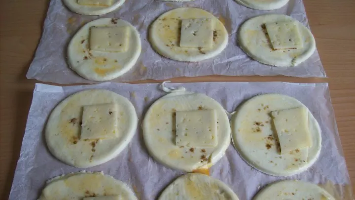 Die entstandenen Teigkreise werden großzügig mit dem Eigelb bestrichen und seitlich mit jeweils einem Stückchen der Käsescheiben belegt. 
