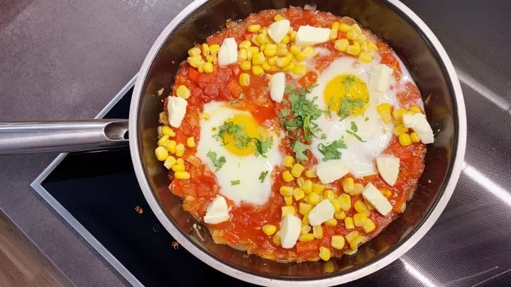Wenn die Eier wachsweich sind, werden Mozzarella und Parmesan zusammen mit den Kräutern auf der auf dem Schakschuka verteilt.