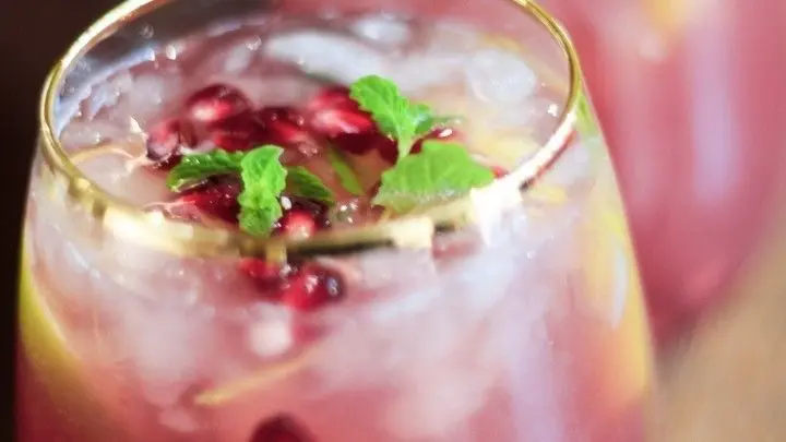 Ein alkoholfreier Weihnachtscocktail mit Granatapfel und Minze steht in eleganten Gläsern auf einem Holztisch, umgeben von festlicher Atmosphäre.