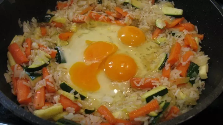 Der gebratene Reis mit dem Gemüse wird an den Rand der Pfanne zusammengeschoben, dann schlägt man die Eier in die Mitte.